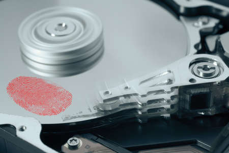Hard disk drive with red fingerprint on surface. The read write head is moving. It is a symbol for...