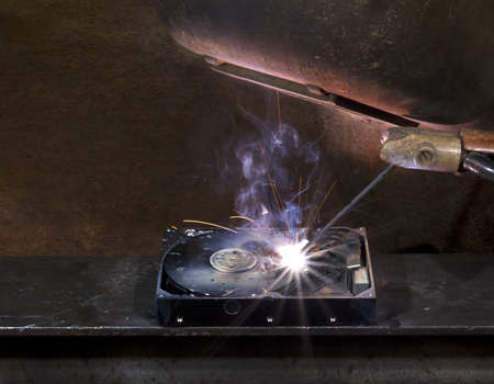 repairing a defect hard disk with welding apparatus. Protective shield and smoke on rusty backgroundの写真素材