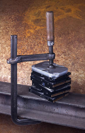 heavy screw clamp giving pressure to several hard drives. Studio shot taken in front of rusty backgroundの写真素材
