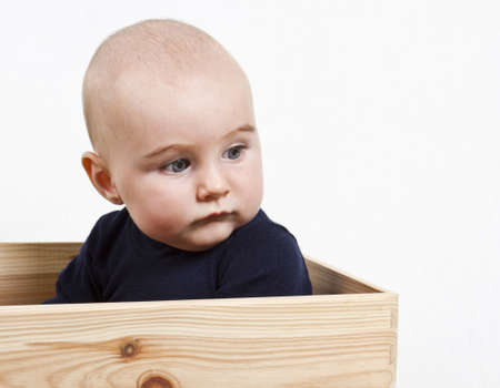 single toddler with dark shirt in wooden box looking to the right.の写真素材
