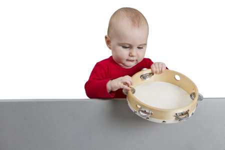 young child holding tambourine behind grey shield. isolate on white backgroundの写真素材