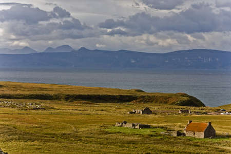 old abandoned houses at scottish coastline with grassland and mountainsの写真素材