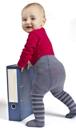 small child in red shirt standing next to blue ring binder. white background with shadow. Looking into towards cameraの写真素材