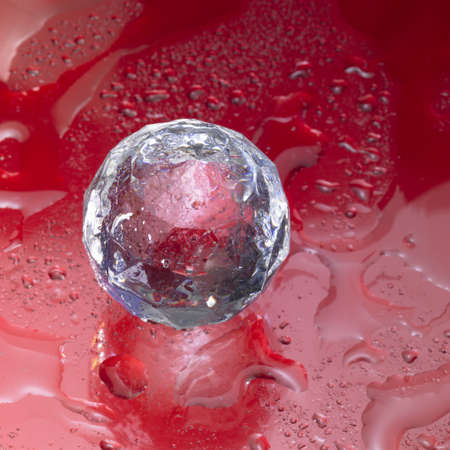 Studio photograpgy of a diamond ball made of glass in red back with water dropsの写真素材