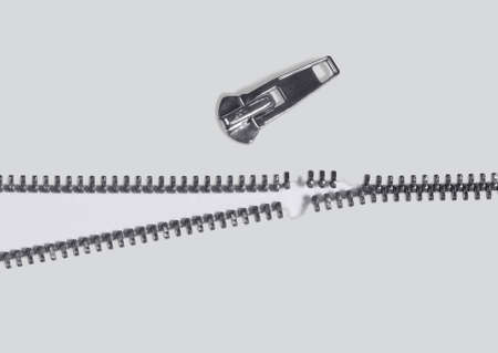 symbolic studio photography of a damaged zipper in light back, seen from aboveの写真素材