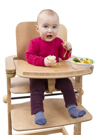 young child in red shirt eating vegetables in wooden chair の写真素材