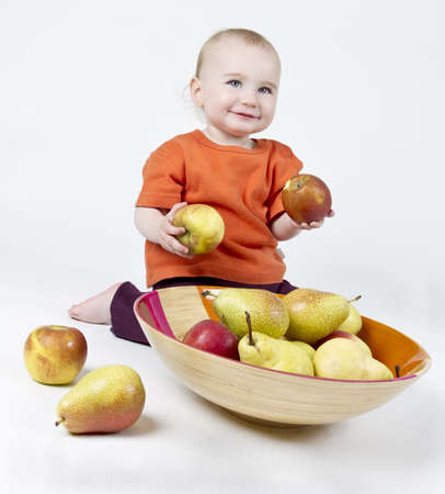 baby with apples and pears laying in bowl - studio shotの写真素材