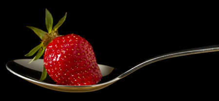 single red, fresh strawberry on spoon in black backgroundの写真素材