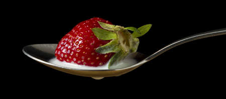 red, ripe strawberry falling in spoon with fresh milk - isolated on lack backgroundの写真素材