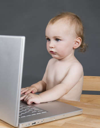 young child with laptop computer on wooden desk in grey backgroundの写真素材
