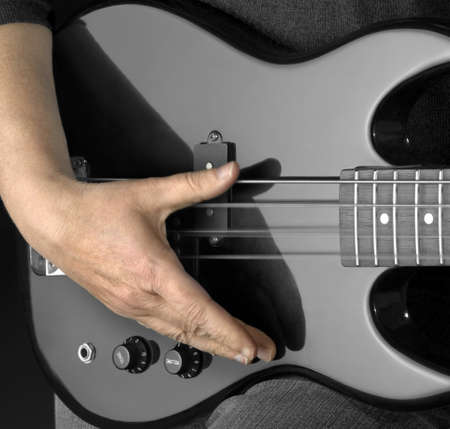 detail of a black bass guitar and hand in dark backの写真素材
