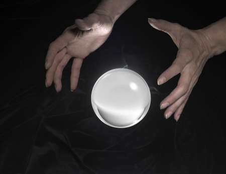 high angle shot of a glowing crystal ball surrounded by black crinkly fabrics and two hands aroundの写真素材