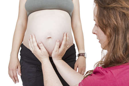 young midwife fingering at human belly  pregnant woman standing while midwife is sitting in front  horizontal picture isolated on whiteの写真素材