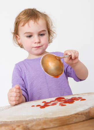 child putting sieved tomatoes on dough  studio shot in grey backgroundの写真素材