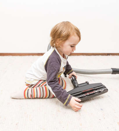 young child sitting next to vacuum cleanerの写真素材