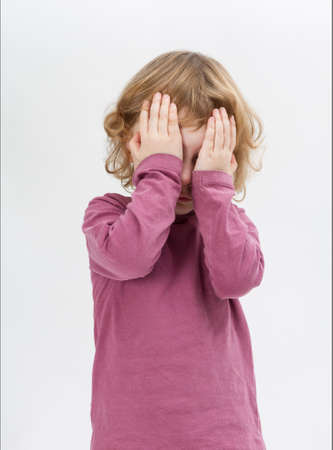 child covering eyes with hands. studio shot in grey background