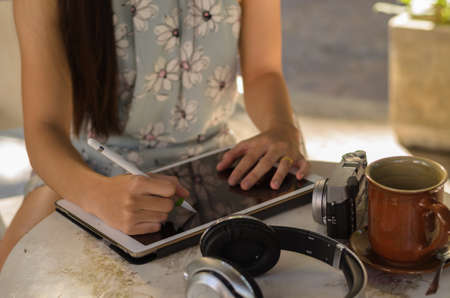 Woman use hand hold pen working in tablet,earphone and camera put on the tableの写真素材