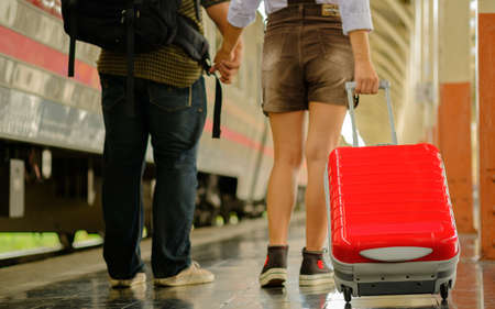 Woman and man hold hands walk in train station go travel drag bag red color,blur background,の写真素材