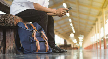 Asian men are using mobile phones while waiting for trains,With a black bag placed beside and copy...