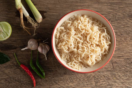 A cup of instant noodles placed on a wooden table With lime, chilli, lemon grass and garlic as ingredients, top view noodleの写真素材