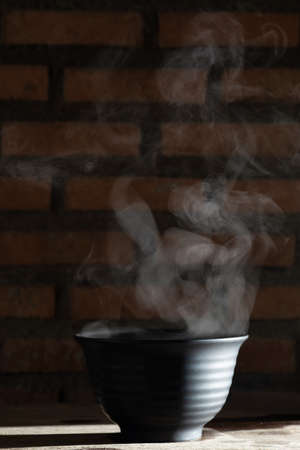Soup hot in black bowl on wooden table, food steam and copy space, selective focusの写真素材