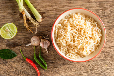 A cup of instant noodles placed on a wooden table With lime, chilli, lemon grass and garlic as ingredients, top view noodleの写真素材