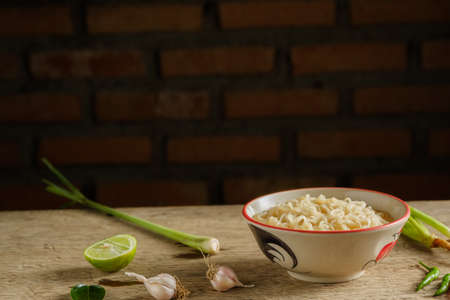 A cup of instant noodles placed on a wooden table With lemons, lemon  grass  and garlic as ingredients. copy spaceの写真素材