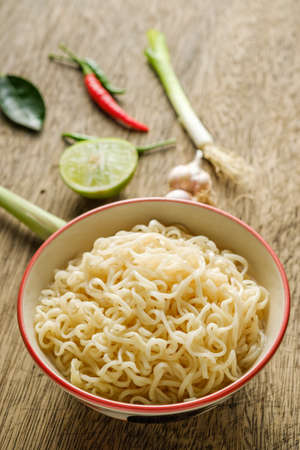 A cup of instant noodles placed on a wooden table With lime, chilli, lemon grass and garlic as ingredients, top view noodleの写真素材
