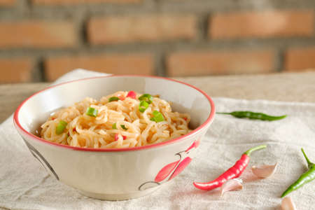 A cup of instant noodles placed on a wooden table With chilli as ingredientsの写真素材