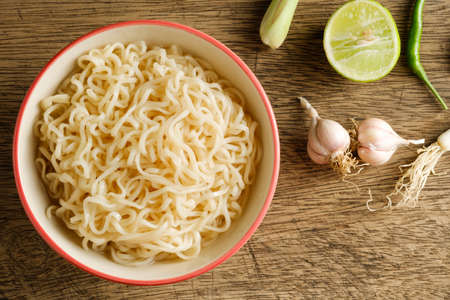 A cup of instant noodles placed on a wooden table With lime, chilli, lemon grass and garlic as ingredients, top view noodleの写真素材