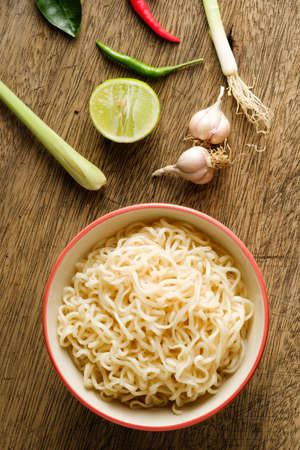 A cup of instant noodles placed on a wooden table With lime, chilli, lemon grass and garlic as ingredients, top view noodleの写真素材