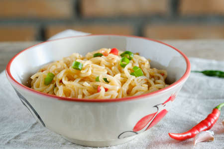 A cup of instant noodles placed on a wooden table With chilli as ingredientsの写真素材