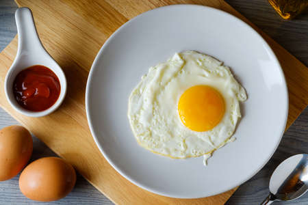 The fried egg is in a white round dish placed on a cutting board,top view food conceptの写真素材