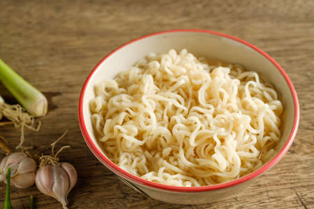 A cup of instant noodles placed on a wooden table With lemon grass and garlic as ingredientsの写真素材
