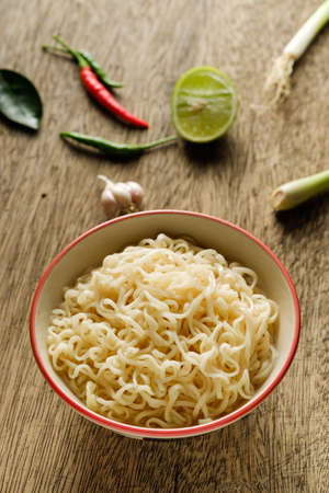 A cup of instant noodles placed on a wooden table With lime, chilli, lemon grass and garlic as ingredients, top view noodleの写真素材