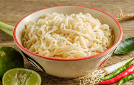 A cup of instant noodles placed on a wooden table With lime, chilli, and garlic as ingredientsの写真素材