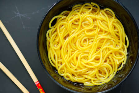 The noodles are in a bowl  placed on table.yellow noodle in black bowl.の写真素材