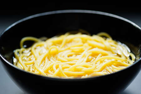 The noodles are in a bowl  placed on table.yellow noodle in black bowl.