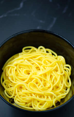 The noodles are in a bowl  placed on table.yellow noodle in black bowl.の写真素材