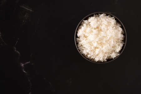 The rice is cooked in a plastic cup on a dark background.A cup of rice is placed on the backdrop with copy space.の写真素材
