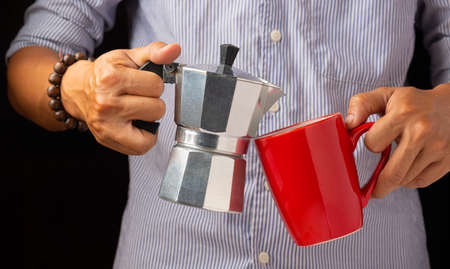 The right hand holds the coffee pot and the other hand holds the red coffee cupの写真素材