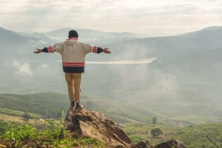 Man standing with arms outstretched on a rock with mountain scenery.man standing with arms outstretched on stone and copy spaceの写真素材
