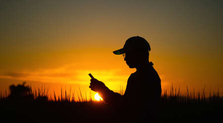 Men wearing striped shirts with a cap stand to use the phone At sunset with copy space.Silhouette of a man in a hat using a phoneの写真素材
