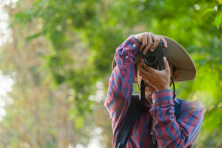 Asian man holding a camera with both hands.man wearing a hat taking pictures,copy space.の写真素材