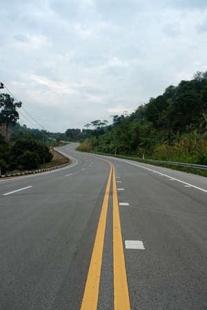 Paved road curve on mountains.Road dividing line.The road to the mountain.The asphalt road on both sides of the road is covered with grass.の写真素材