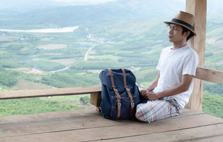 Asian man sleeping and relaxing.A man wearing a white shirt and striped pants wears a straw hat.copy space,Happy travelers relax with forest and mountain views. travel and leisureの写真素材