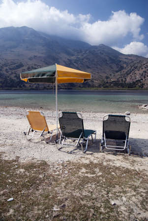 Three deck chairs and umbrellas on the background of the sea and mountainsの写真素材
