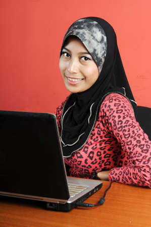 Beautiful young muslim smile infront of notebook isolated red wallの写真素材