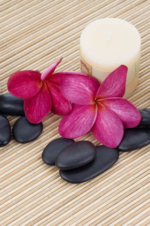 Red frangipani on bamboo mat with rock and candleの写真素材