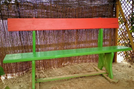 Wooden bench painted in green and orange in shaded areaの写真素材